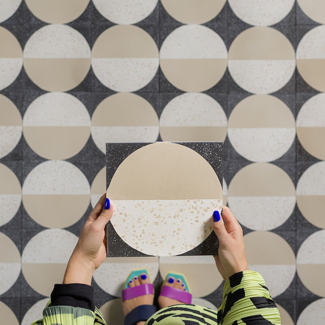 Square cement tile featuring a modern geometric design with a half-beige and half-white terrazzo circle on a dark speckled background, ideal for contemporary flooring and wall décor.