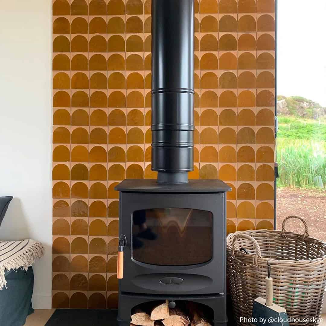 A cozy indoor scene with a black wood-burning stove on a black hearth, storing chopped firewood underneath.