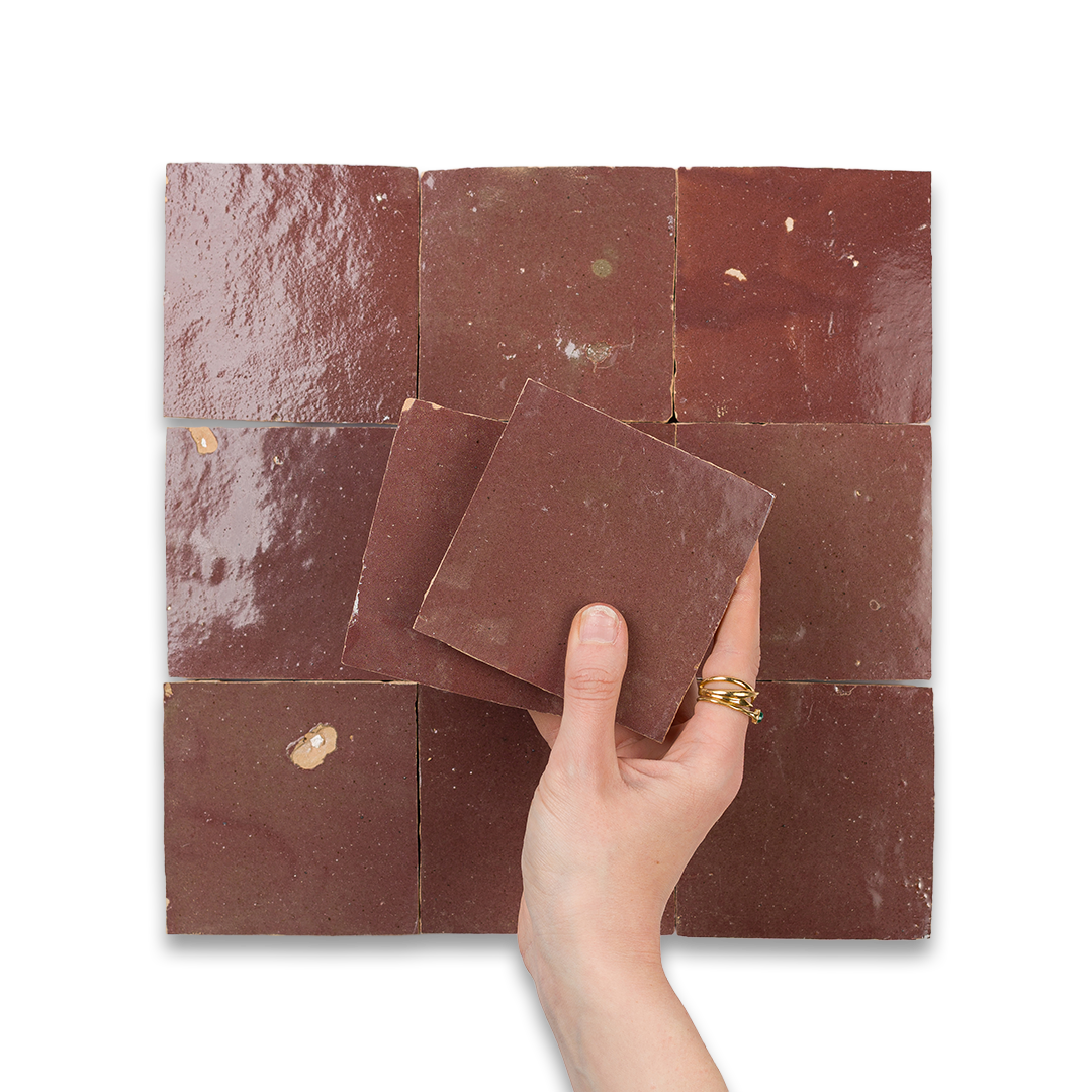 Hand holding a brown square tile against a patterned tile background