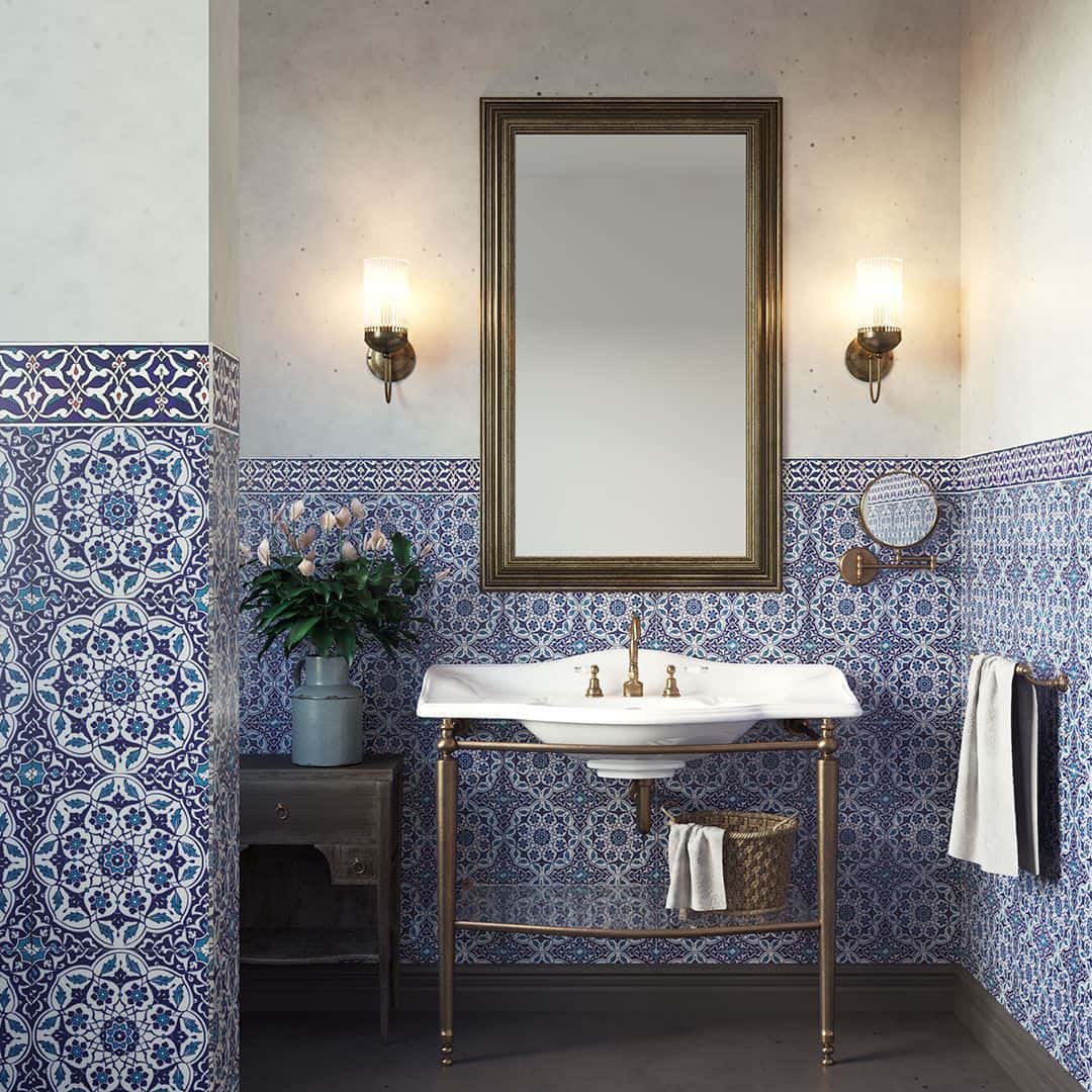 Elegant bathroom vanity with brass fixtures, framed mirror, and blue patterned tile walls in a classic design.