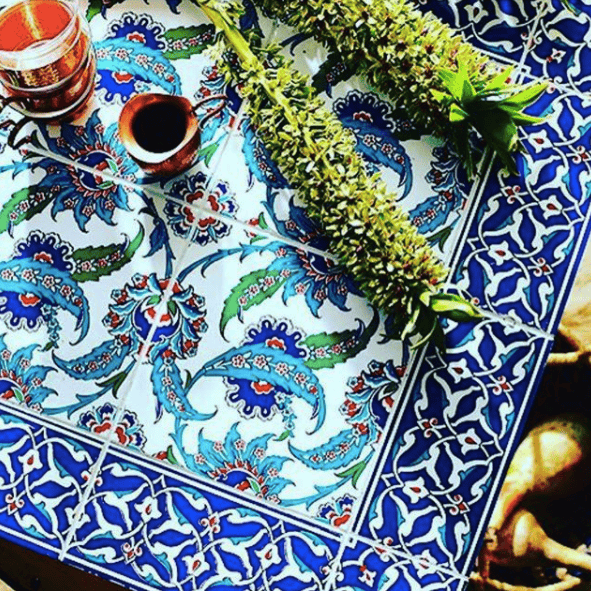 Decorative tabletop with vibrant blue, red, and green patterned tiles, styled with herbs and a small coffee cup.