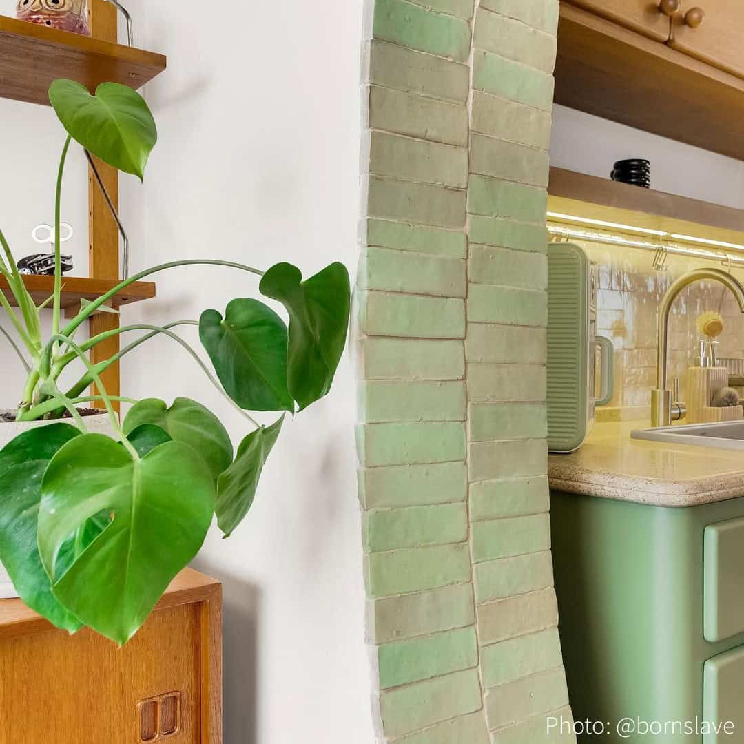 Retro kitchen with arched green tiles, warm lighting, yellow backsplash, and vintage wooden cabinets.