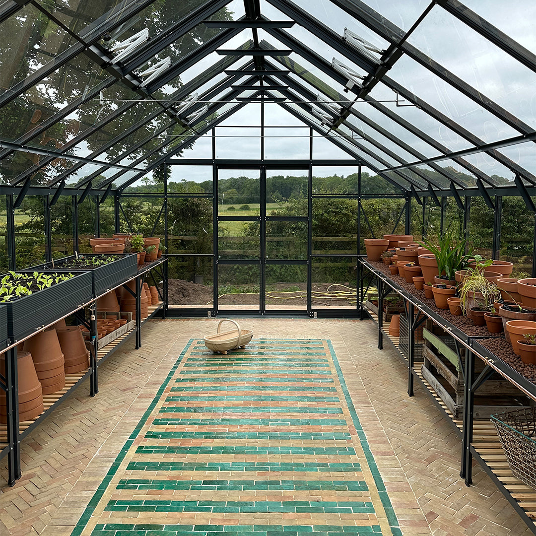 Greenhouse interior with terracotta pots, a rug, and a view of trees outside.