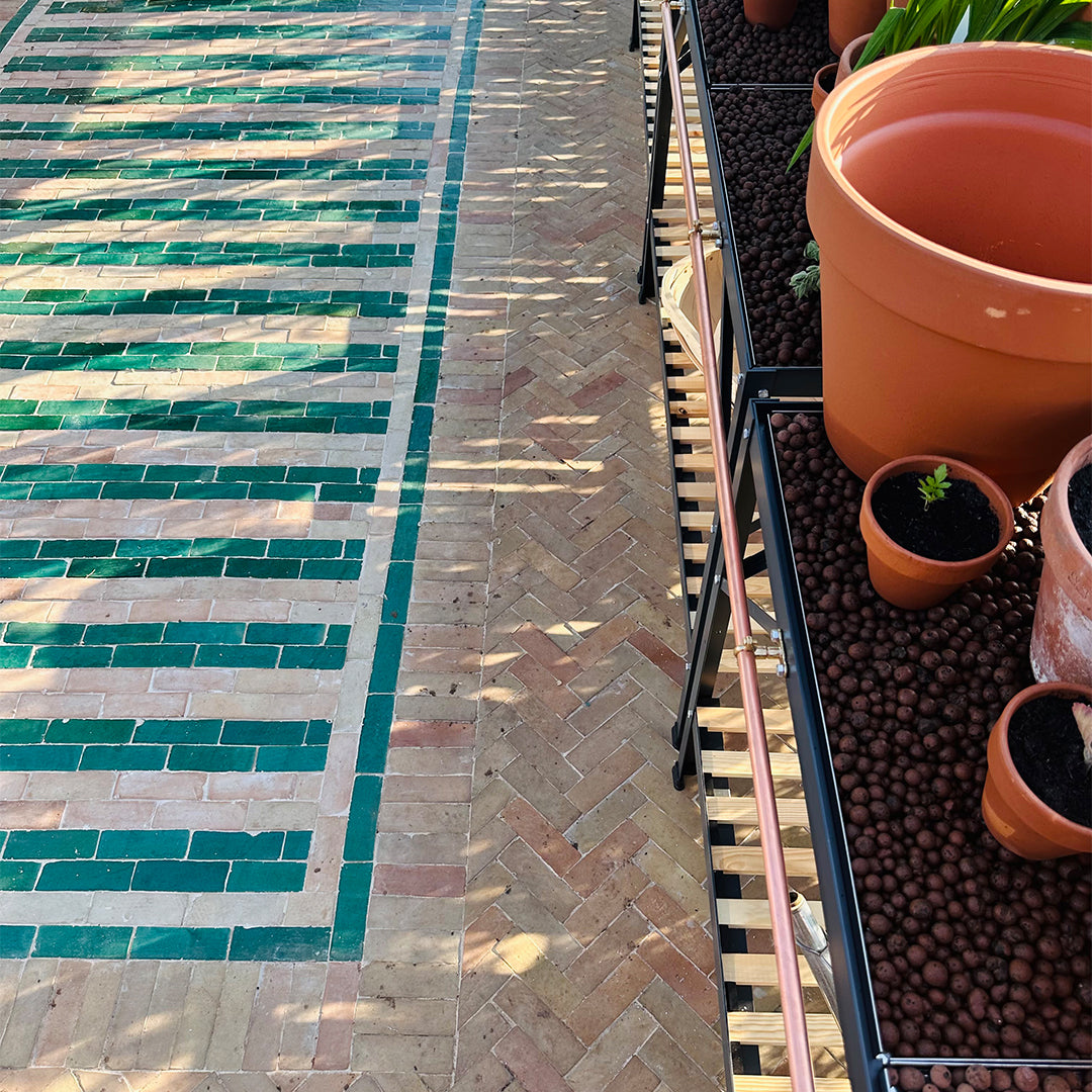 Outdoor patio with tiled and brick patterns, potted plants, and a hose.