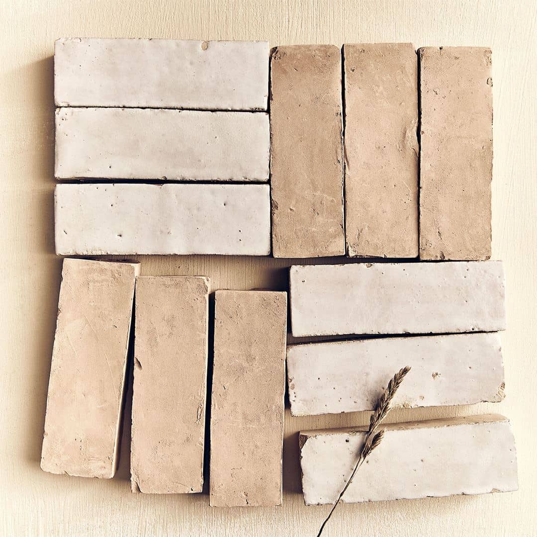 A flat lay of terracotta tiles arranged in a pattern with some white tiles, featuring a single dried plant stem for decoration.