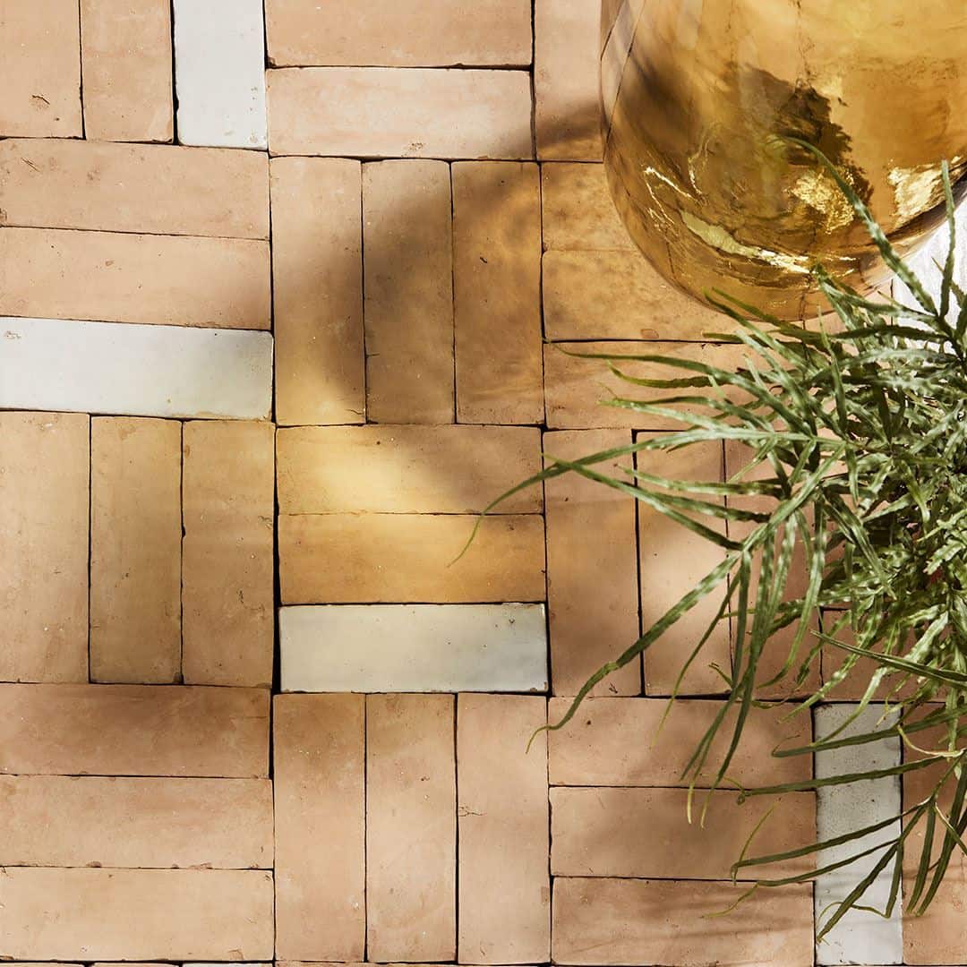 Close-up of a terra cotta tile floor with white accents, featuring a potted plant and a glass vase.