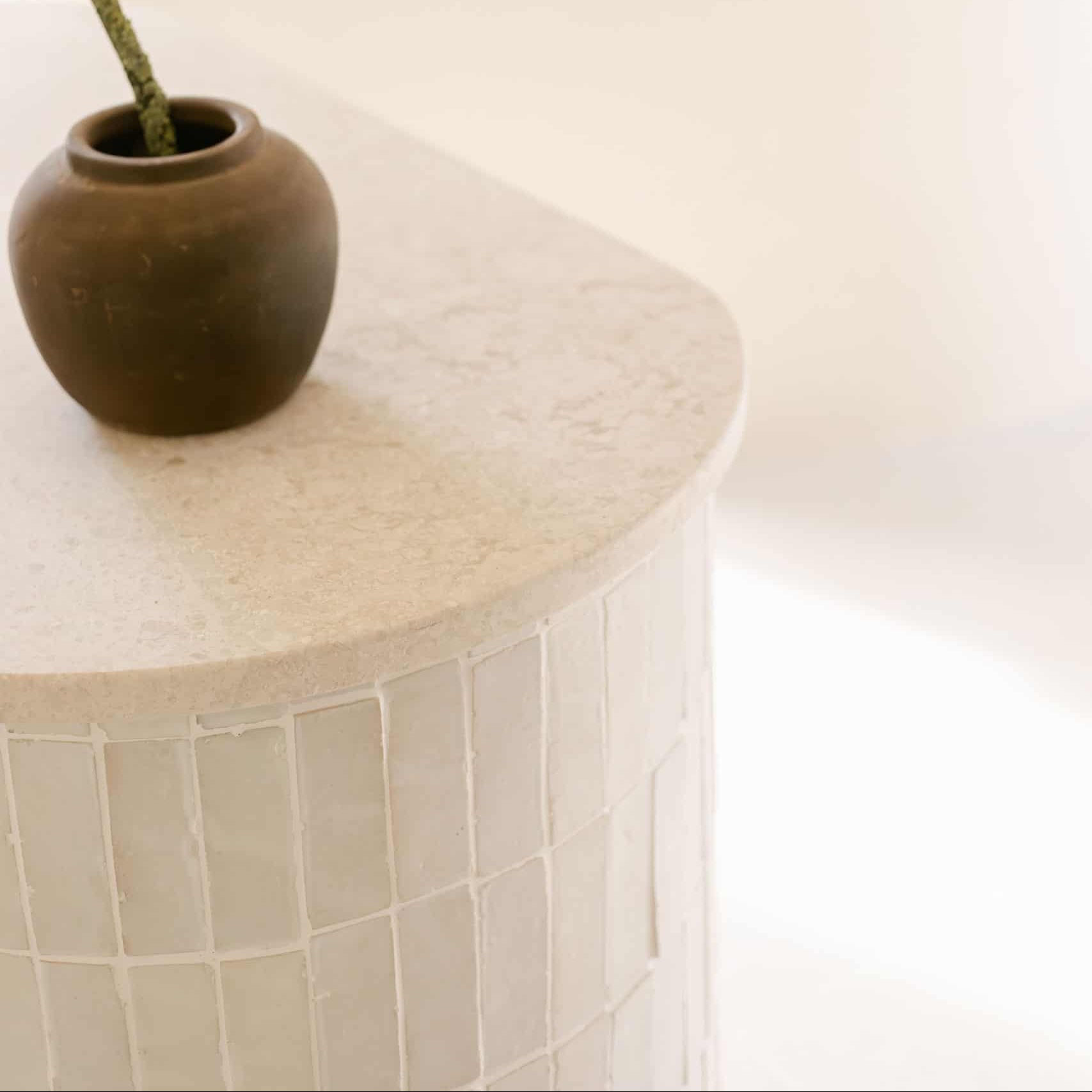 Round stone table with a brown pot on top against a white wall.
