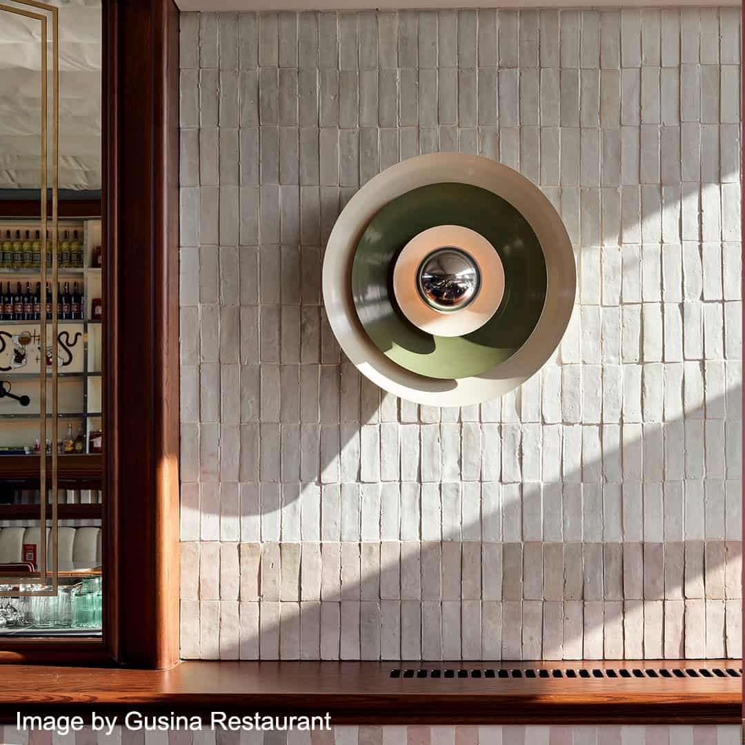 Modern wall light fixture with concentric circular layers in white, green, and metallic tones mounted on a textured beige tile wall
