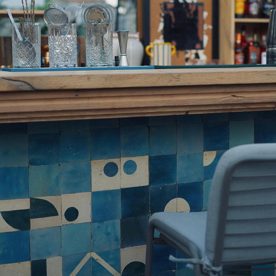 Bar counter with blue tiled wall and a chair in a bar setting