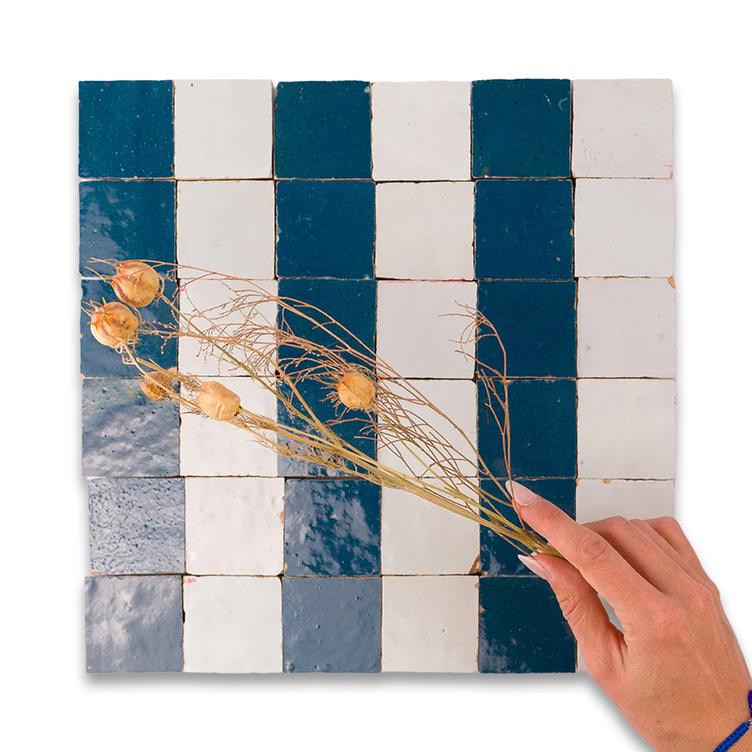 Hand holding a dried plant over a checkered tile pattern