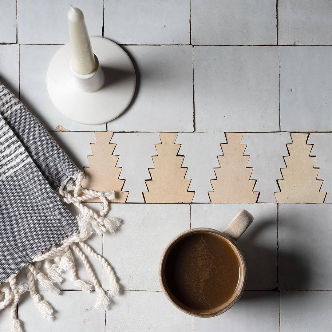 Flat lay with gray tiles, zigzag beige pattern, striped fabric, candle, and ceramic mug of coffee