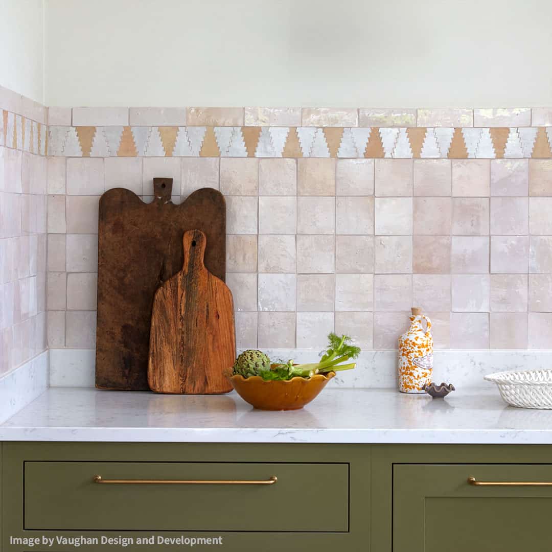 Kitchen countertop with beige tiled backsplash, wooden boards, yellow bowl of vegetables, and olive cabinetry.