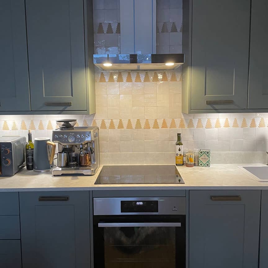 Modern kitchen with teal cabinets, beige countertop, patterned backsplash, and stainless range hood.