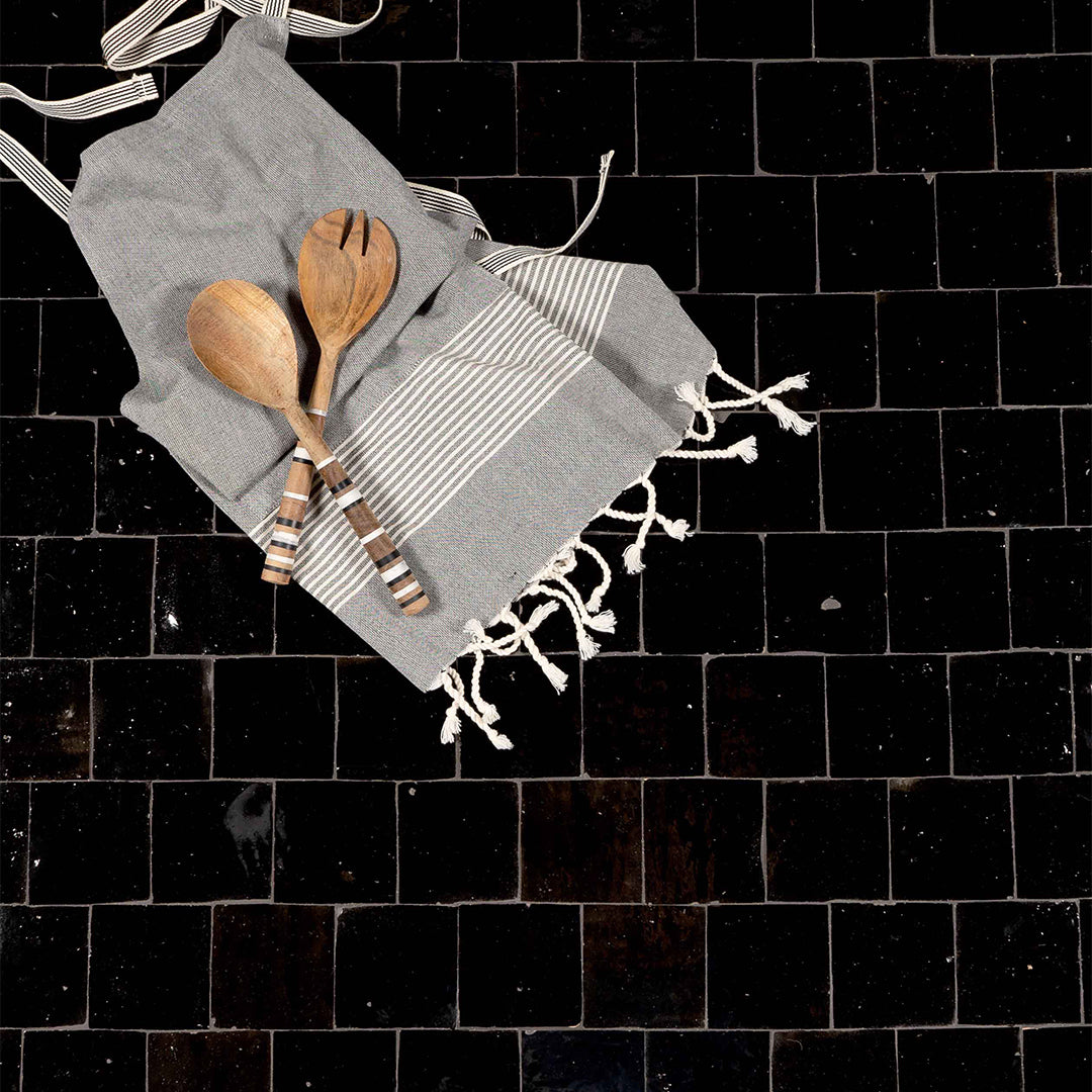 Gray towel with white fringes and wooden spoons on a black tiled surface