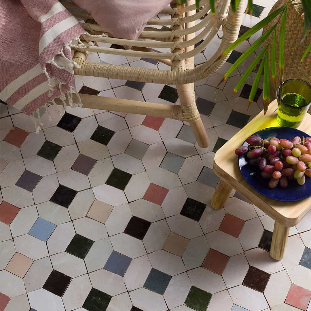 Hexagonal tiled floor with a wicker chair and small table holding grapes.