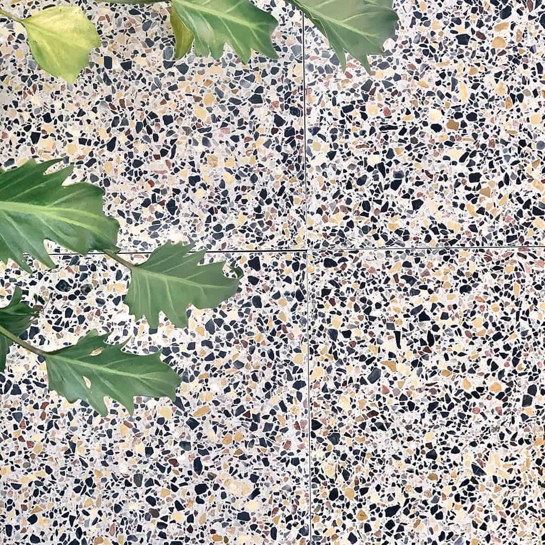 neutral terrazzo tile surface with multicolored stone chips in beige, black, gray, and warm earthy tones.