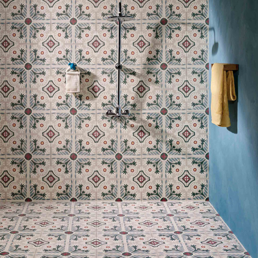 Decorative floral patterned tile shower with wall-mounted fixtures, matching floor tiles, and blue accent wall with towel.