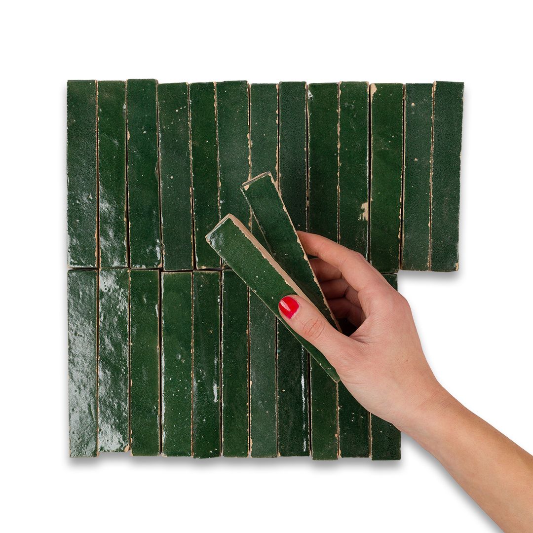 Hand holding a green rectangular tile against a matching tiled wall.