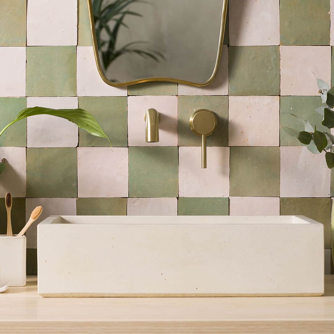 Modern bathroom with green and pink checkered tiles, minimalist sink, and gold faucet fixtures.