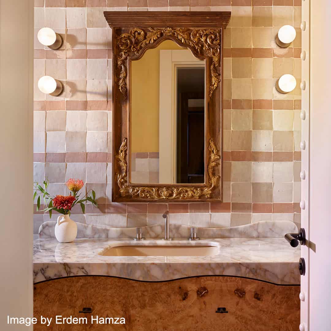 A bathroom vanity with a marble countertop and built-in sink. Above hangs an ornate carved wooden mirror frame with intricate detailing.