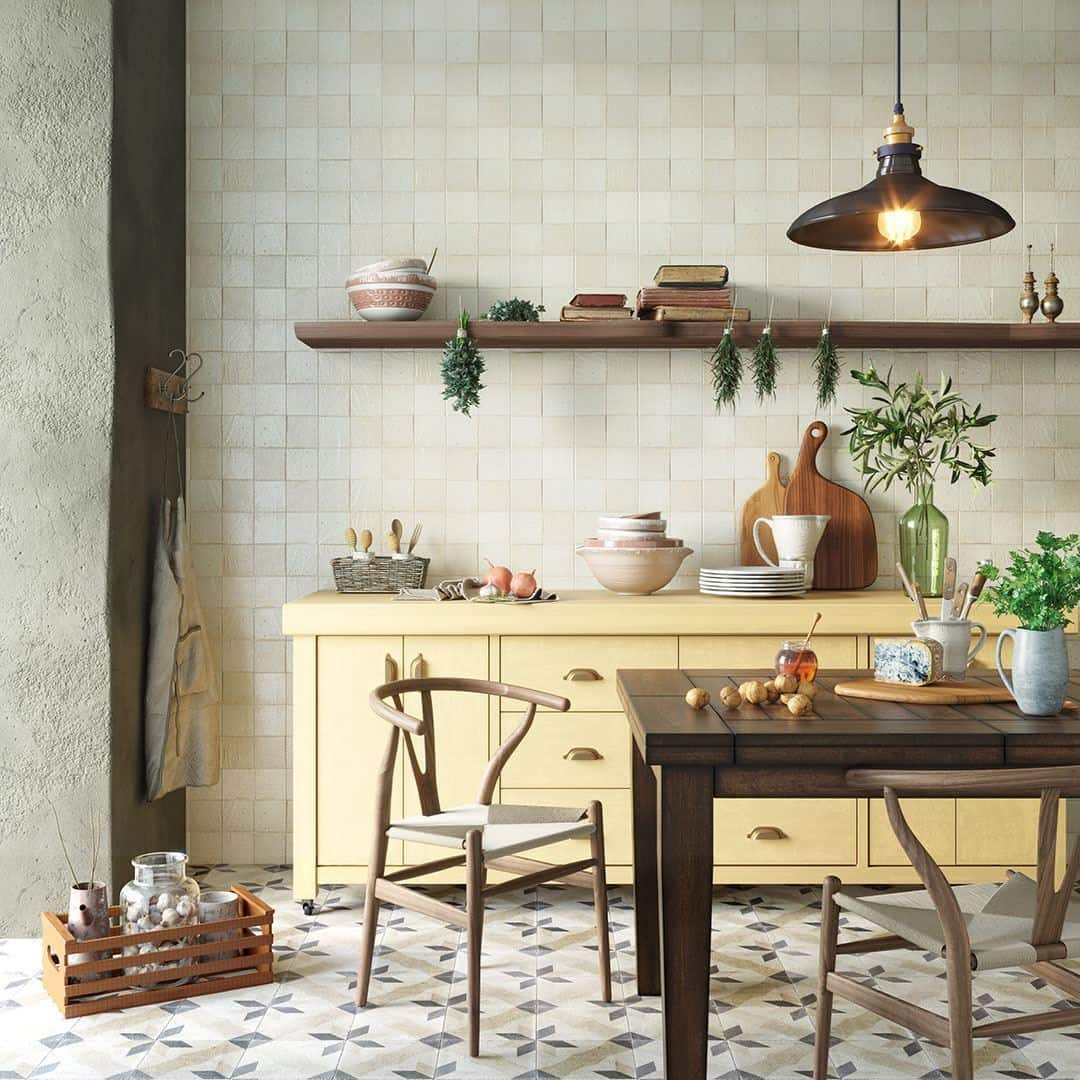 A rustic kitchen interior with a wooden dining table and two chairs, a light yellow sideboard, and a floating wooden shelf above.