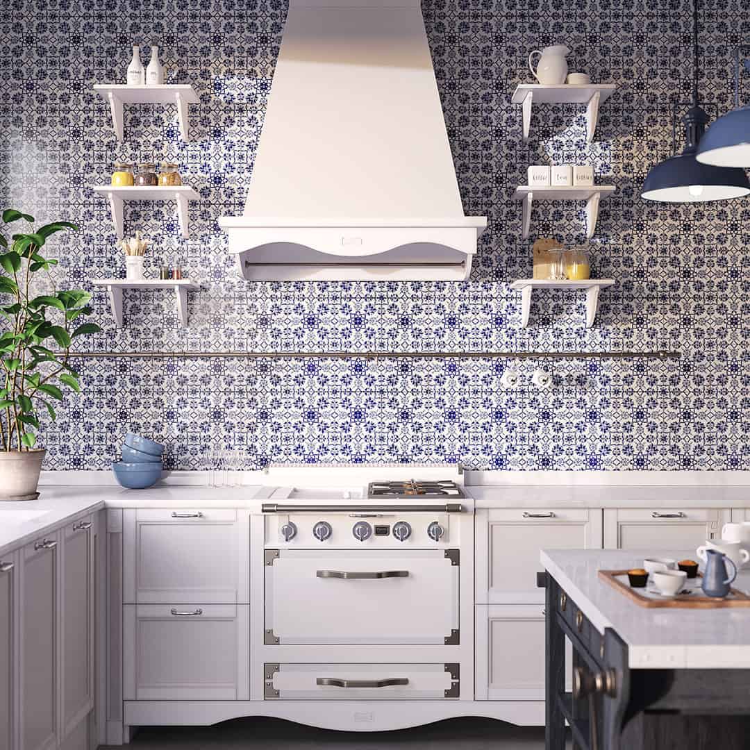 Modern kitchen with blue and white patterned tile backsplash, white stove and range hood, wall shelves with jars and pitcher, white countertop with bowls and cups, and dark blue pendant light above island.