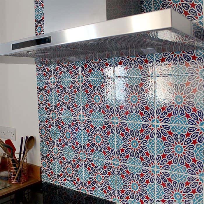 Kitchen with colorful patterned tile backsplash behind stove, stainless hood, and wooden countertops with utensils.