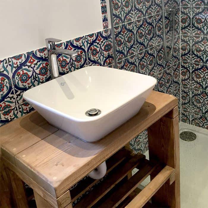 Decorative bathroom with ceramic basin and faucet, ornate blue-red patterned tile wall, wooden counter.