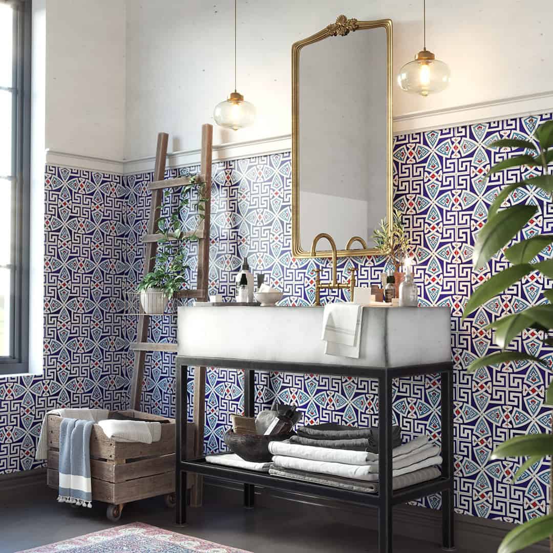 Stylish bathroom with blue patterned tile walls, modern vanity, gold mirror, pendant lighting, and decorative ladder shelf.