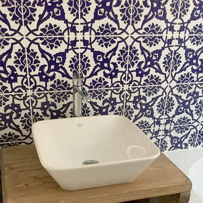 White vessel sink on wood vanity with intricate blue and white patterned tile backsplash in a bathroom setting.