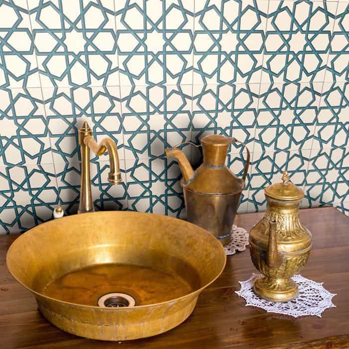 Brass vessel sink with vintage fixtures and Moroccan-style blue geometric tile backsplash on white wall.