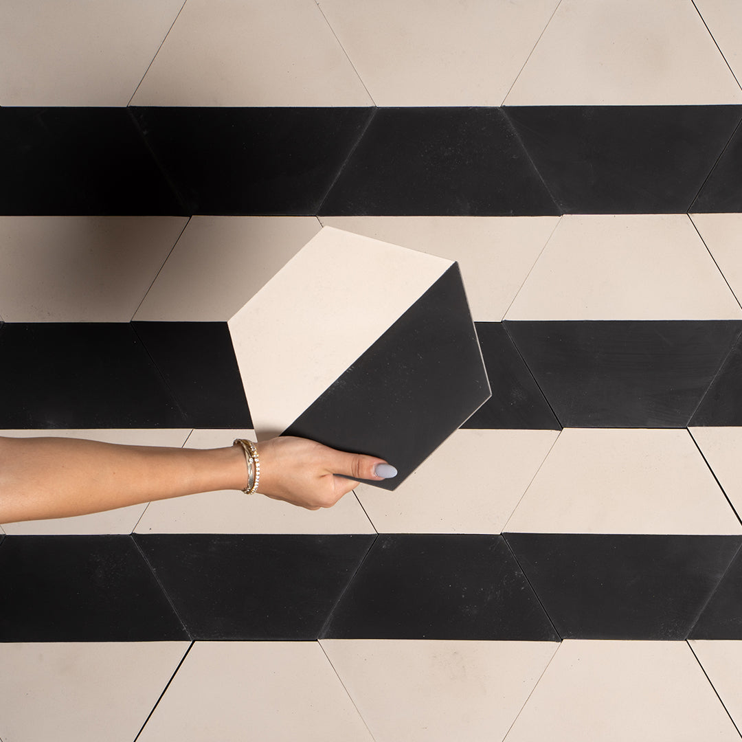 Person holding a black square tile on a patterned floor