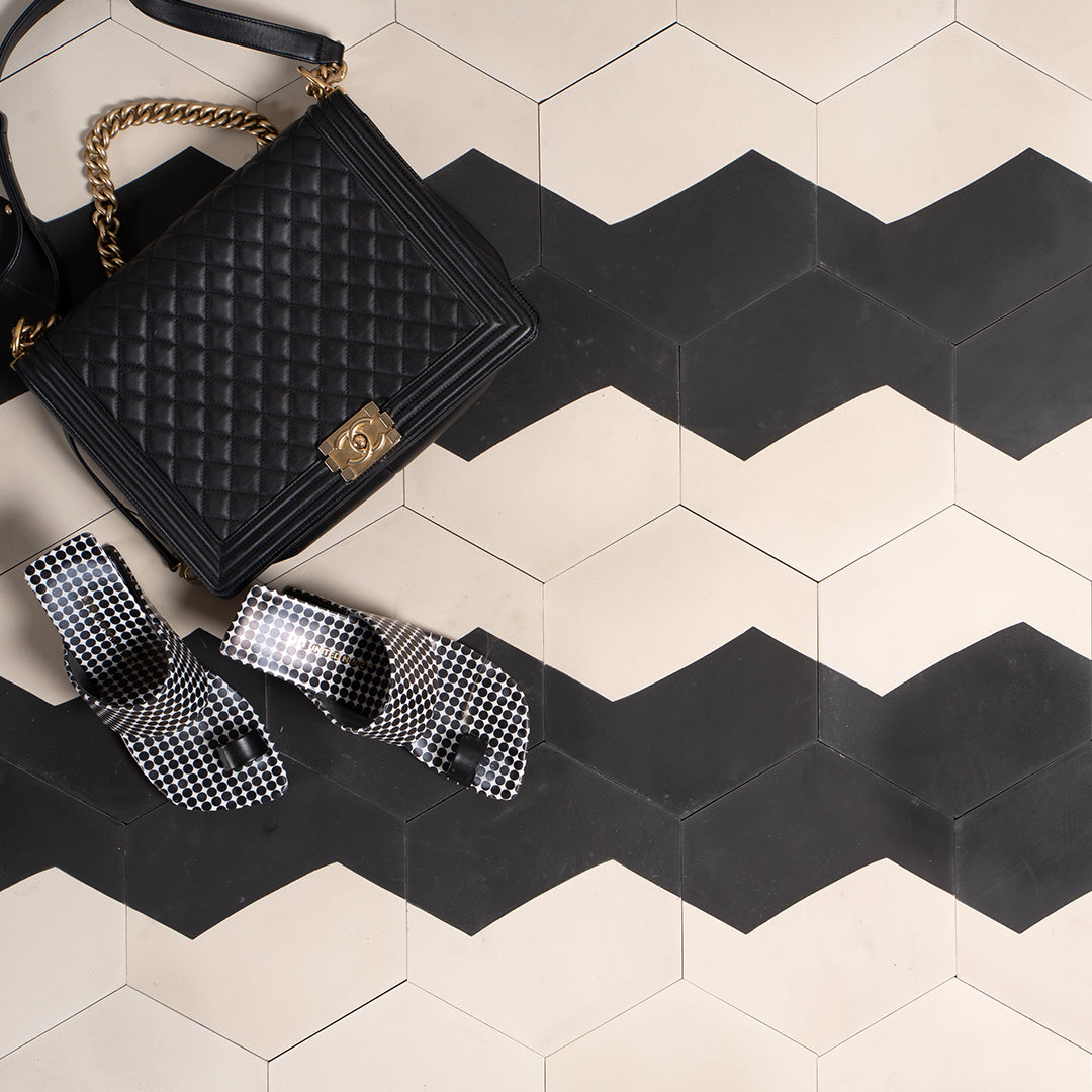 Black quilted handbag with gold chain and bow on a black and white chevron patterned floor.