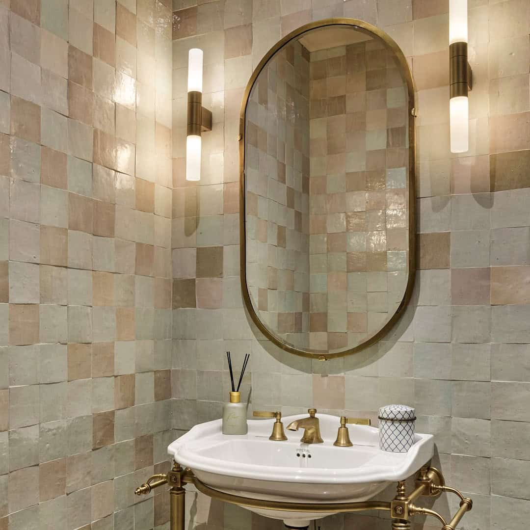 Elegant bathroom with pastel-colored square tiles, a gold-framed oval mirror, and a classic sink with brass fixtures.