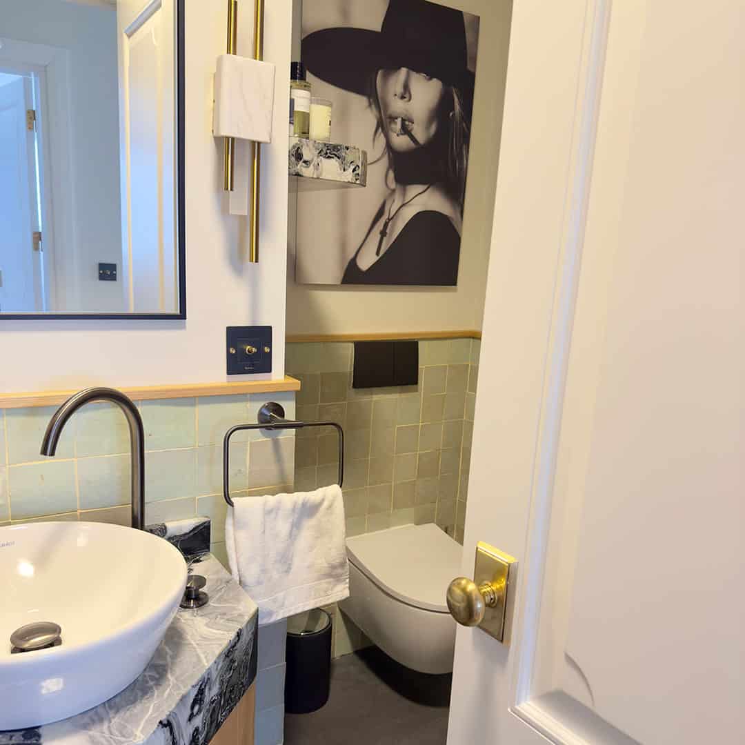 Stylish bathroom with a marble countertop, green tiled walls, a modern sink, and a minimalist toilet. A black-and-white photo and elegant brass fixtures add a chic touch.