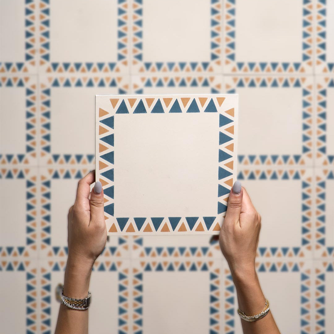 Person holding a square tile with geometric pattern against a tiled wall.