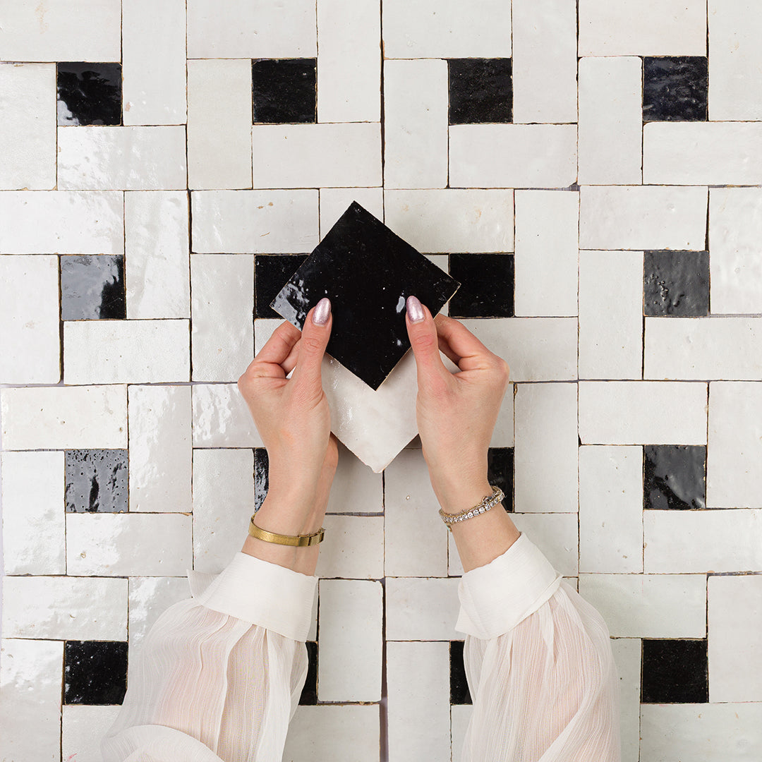 Person holding a black square tile against a patterned wall.