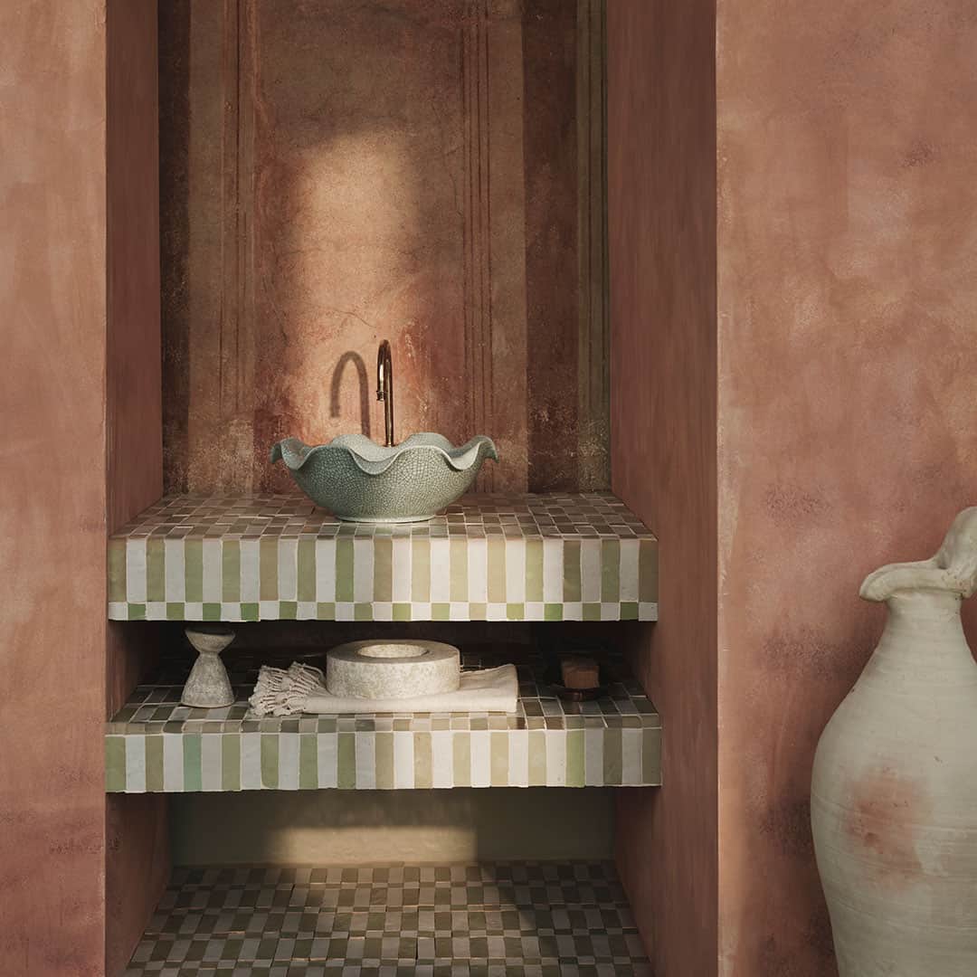A serene bathroom scene featuring a green ceramic sink with a unique wavy design, placed on striped green and white tiles.