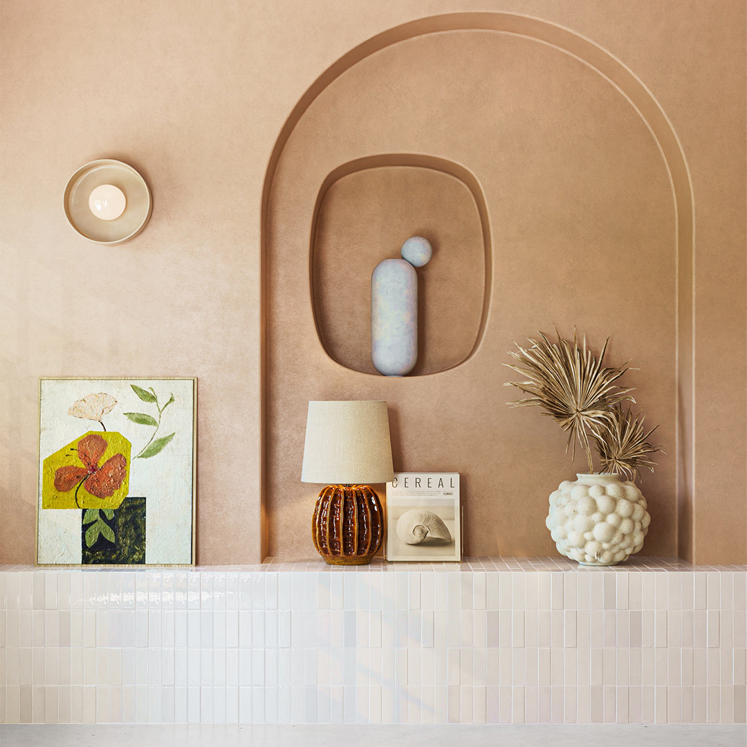 Decorative wall with arch, lamp, vase, and framed picture on a shelf.