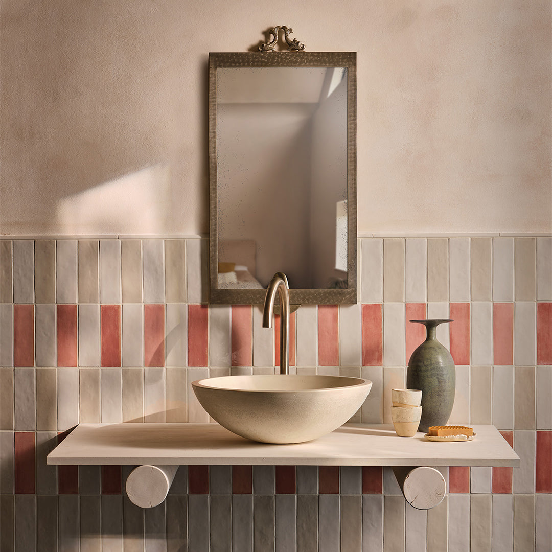 Bathroom with a sink, mirror, and decorative items against a tiled wall.