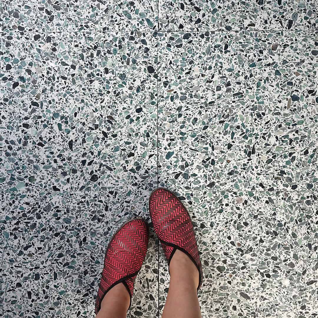 Terrazzo tile floor with green and black stone chips, featuring feet wearing red patterned slip-on shoes.