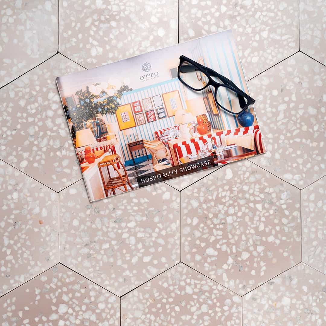 A hexagonal cement tile with a soft blush pink base featuring scattered white and light gray terrazzo-style stone chips, creating a modern, elegant, and textured appearance.