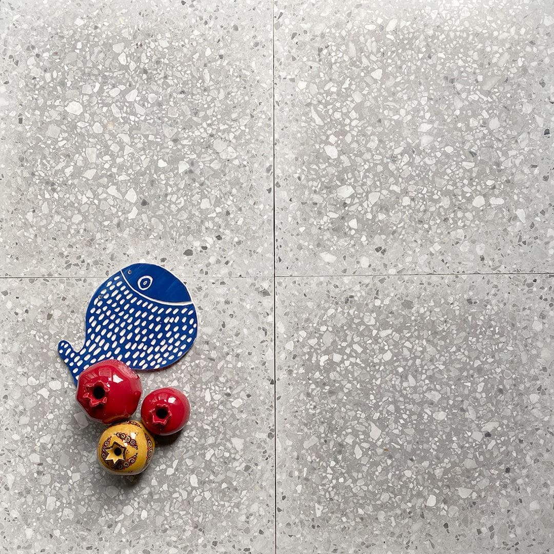 : Light gray terrazzo tile floor with small stone chips, styled with colorful ceramic decor including a blue whale and red ornaments.