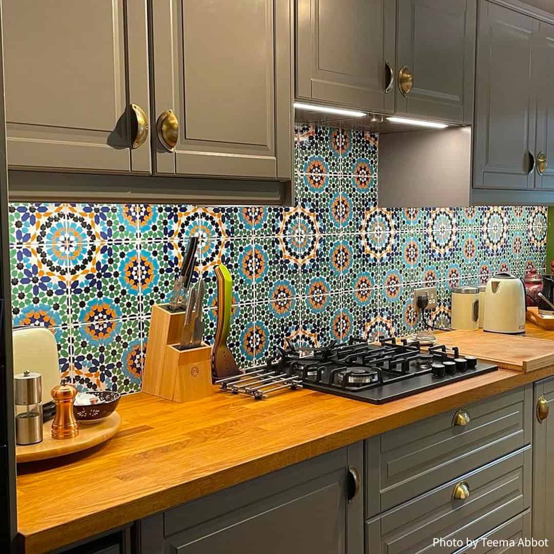 Stylish kitchen with colorful patterned tile backsplash, wooden countertops, grey cabinets, and modern cooking appliances.
