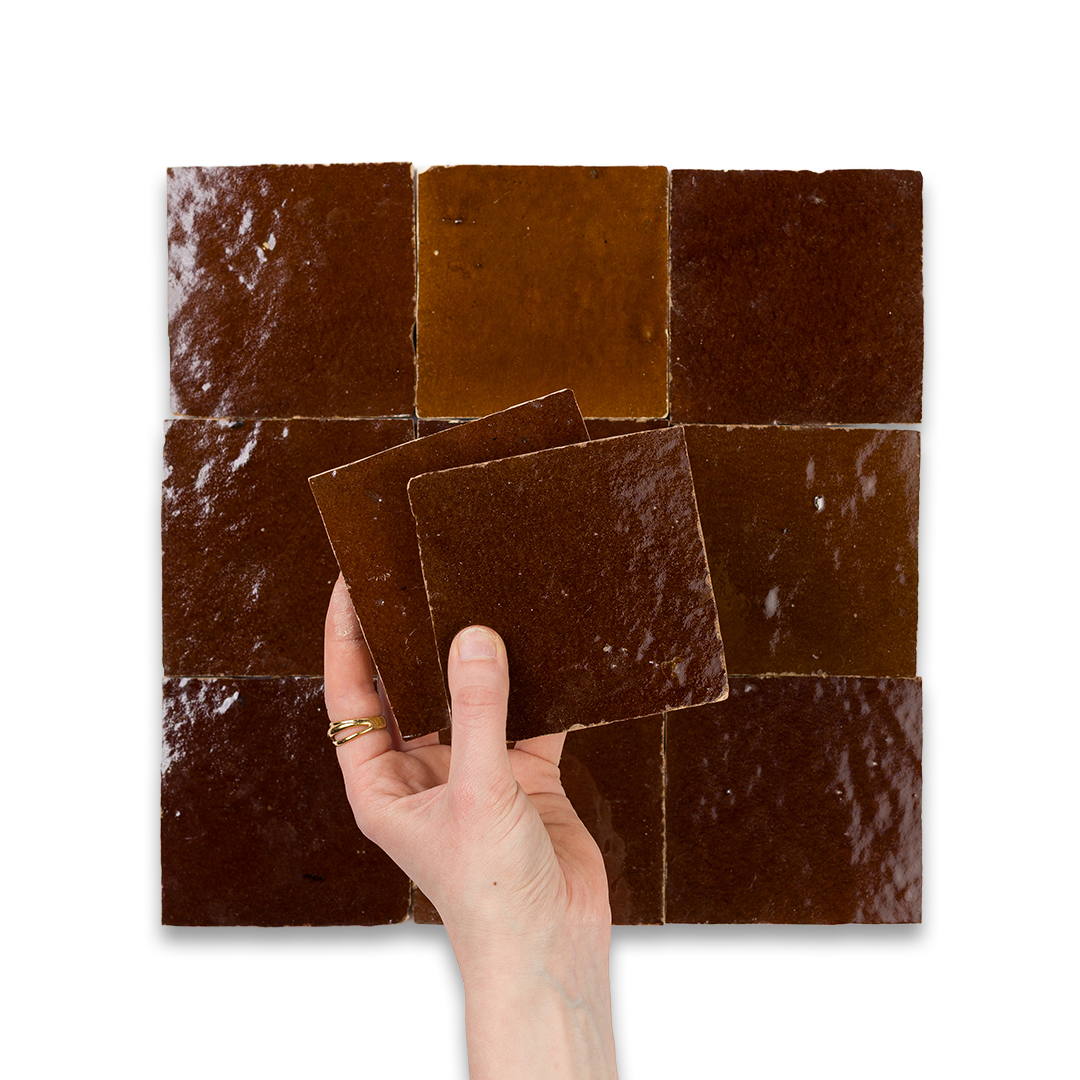 Hand holding a brown square tile against a mosaic background