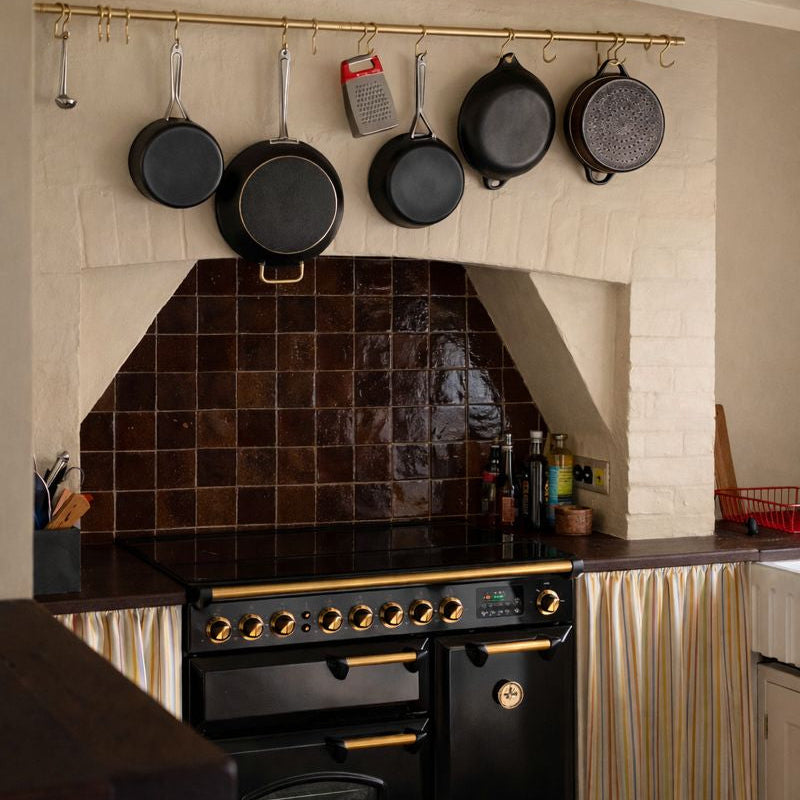 Kitchen with black tiled backsplash, hanging pans, and a stove.