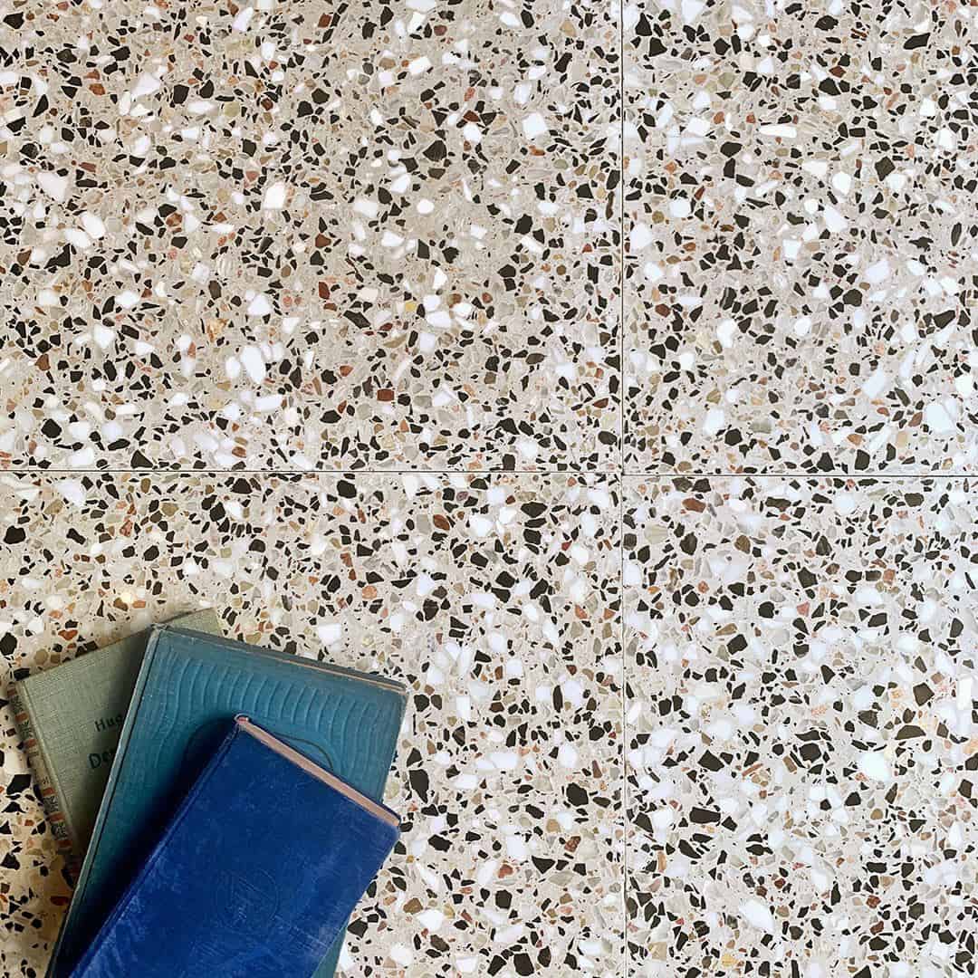 Neutral terrazzo floor tiles with white, black, and tan stone chips, featuring stacked books in the corner.