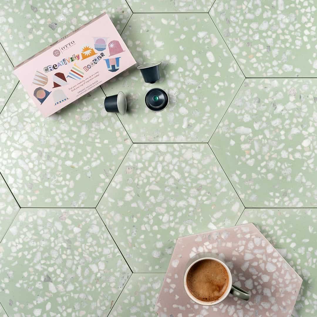 A hexagonal cement tile featuring a soft pastel green base with scattered white and light gray terrazzo stone chips, creating a fresh, modern, and textured decorative design.