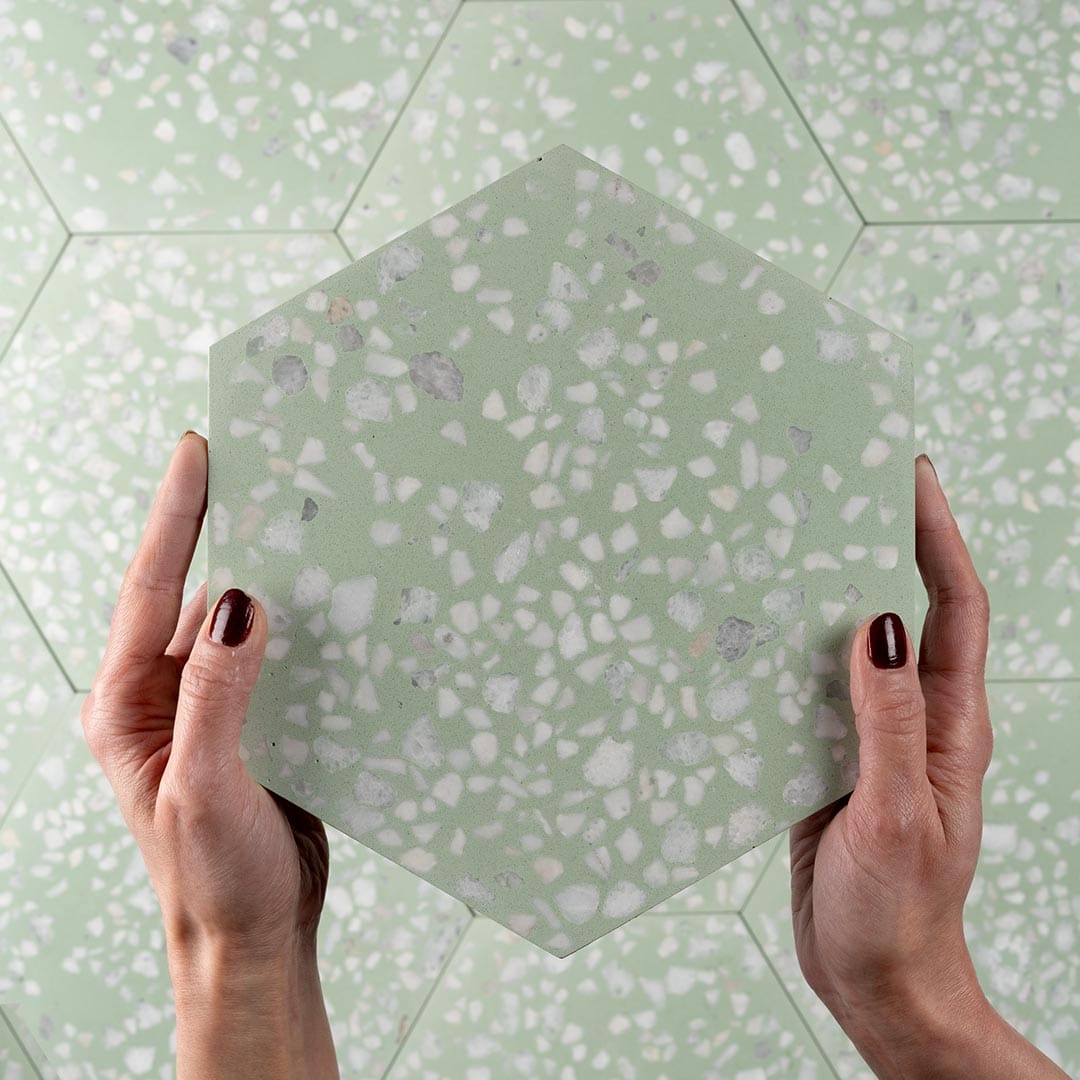 A hexagonal cement tile featuring a soft pastel green base with scattered white and light gray terrazzo stone chips, creating a fresh, modern, and textured decorative design.