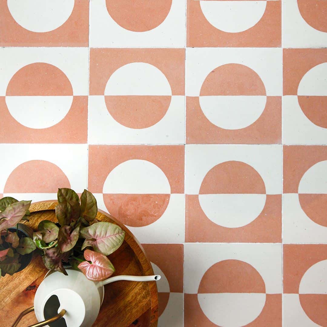 A square cement tile featuring a minimalist geometric design with a terracotta and cream color palette, displaying a half-circle pattern resembling a rising or setting sun.
